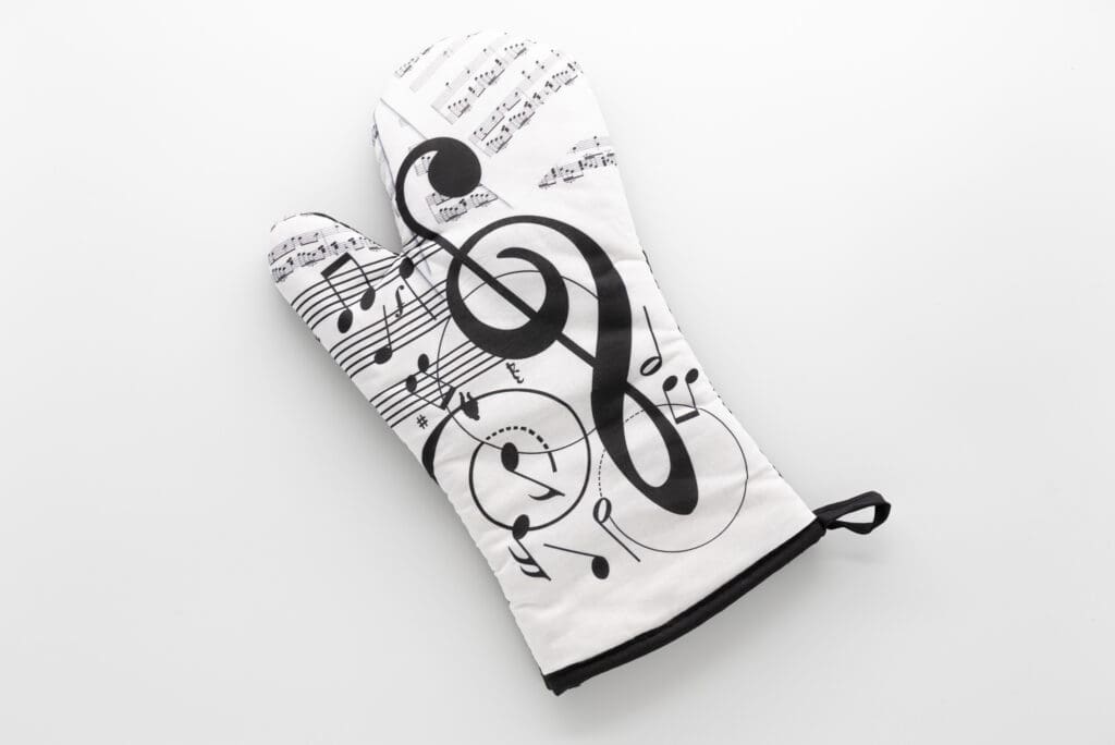 Weißer Topfhandschuh mit schwarzen Musiknoten, Notenlinien und einem großen Violinschlüssel auf der Oberseite.