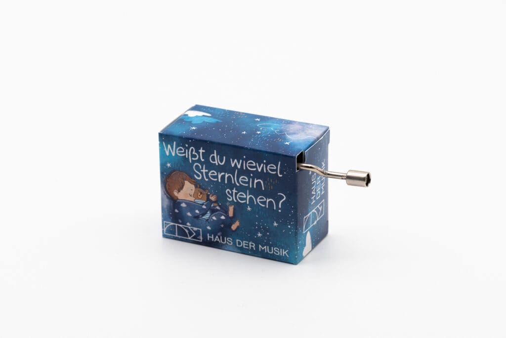 Handkurbel-Spieluhr mit blauem Gehäuse, einer Illustration eines Kindes im Schlafanzug mit Teddybär sowie dem weißen Text "Weißt du wieviel Sternlein stehen?" und dem Logo Haus der Musik.