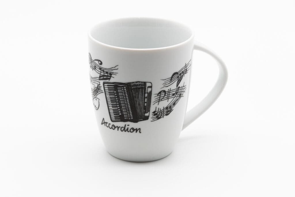 Weiße Tasse mit schwarzen Notenlinien, Notensymbolen und einem gezeichneten Akkordeon sowie dem Schriftzug Accordion auf der Vorderseite.
