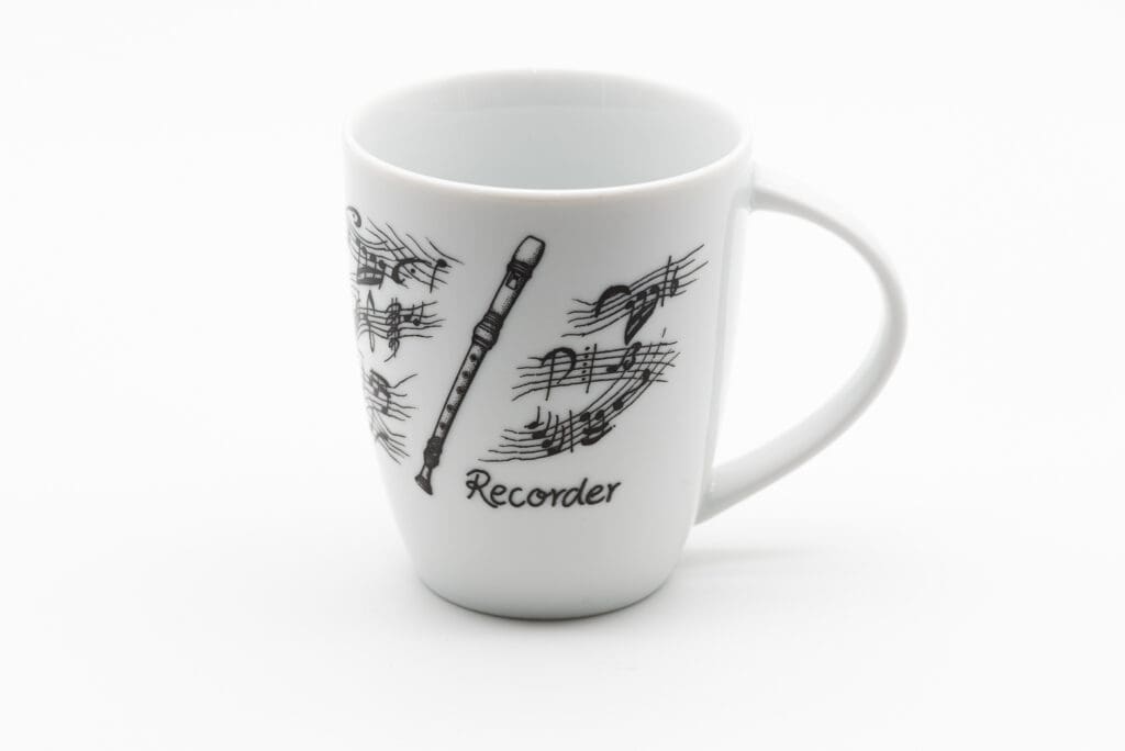 Weiße Tasse mit schwarzen Notenlinien, Notensymbolen und einer gezeichneten Blockflöte sowie dem Schriftzug Recorder auf der Vorderseite.