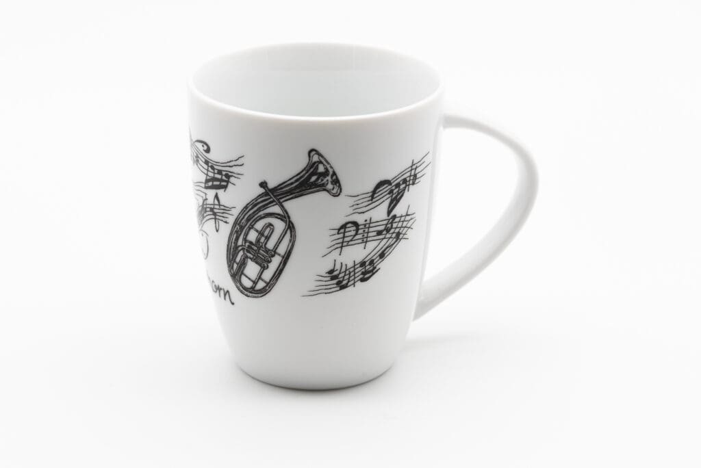 Weiße Tasse mit schwarzen Notenlinien, Notensymbolen und einem gezeichneten Tenorhorn.